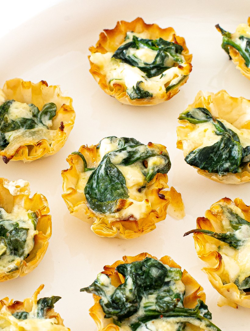 Close up view of spinach phyllo cups on a white serving plate.